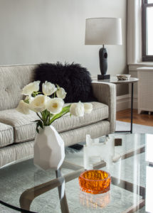 sofa with a furry throw on it behind a vase of white roses