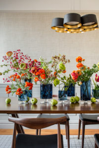 Flowers in vases and apples on a wooden table under a modern chandelier