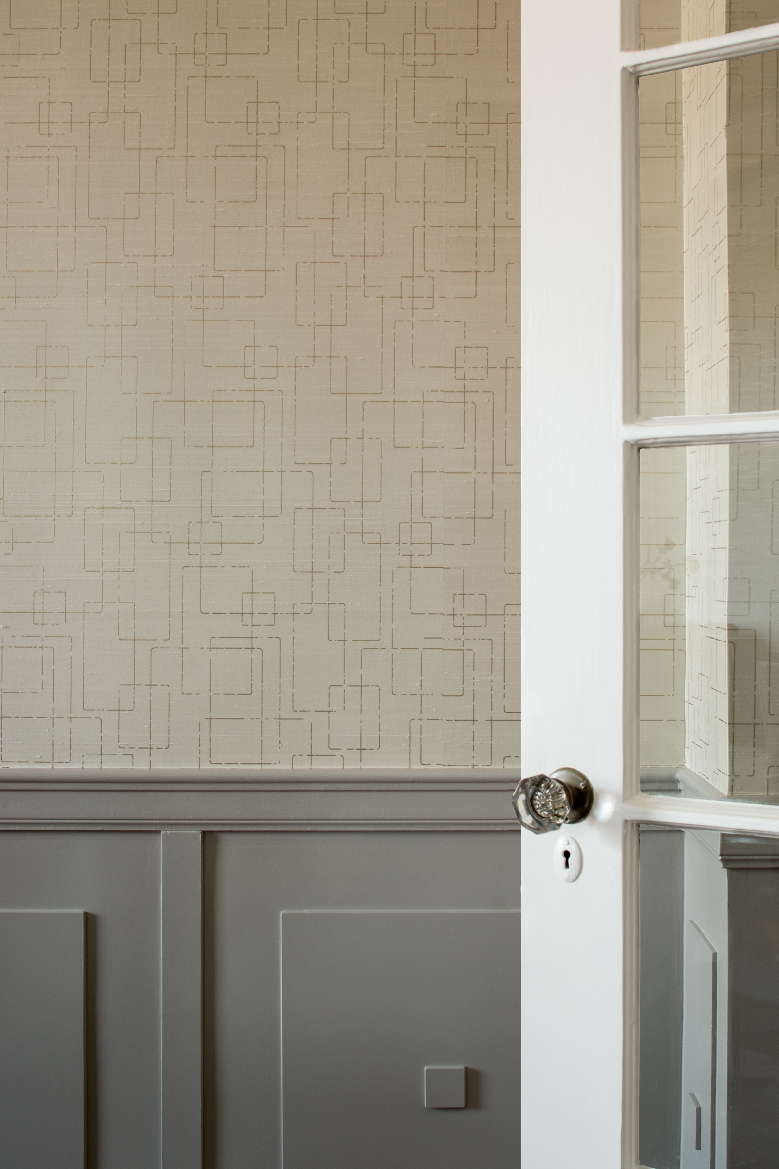 detail of a wallpapered wall with wainscoting and a French door