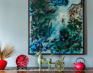 an abstract landscape hanging over a wooden bench with decorative kitchenwares