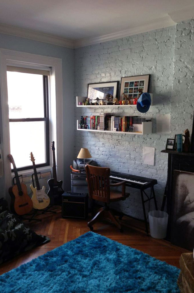 interior of a bedroom with three guitars, a keyboard, and shelves on a brick wall