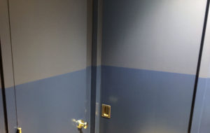 corner of a room with a blue stripe painted on gray walls. there are two doors.