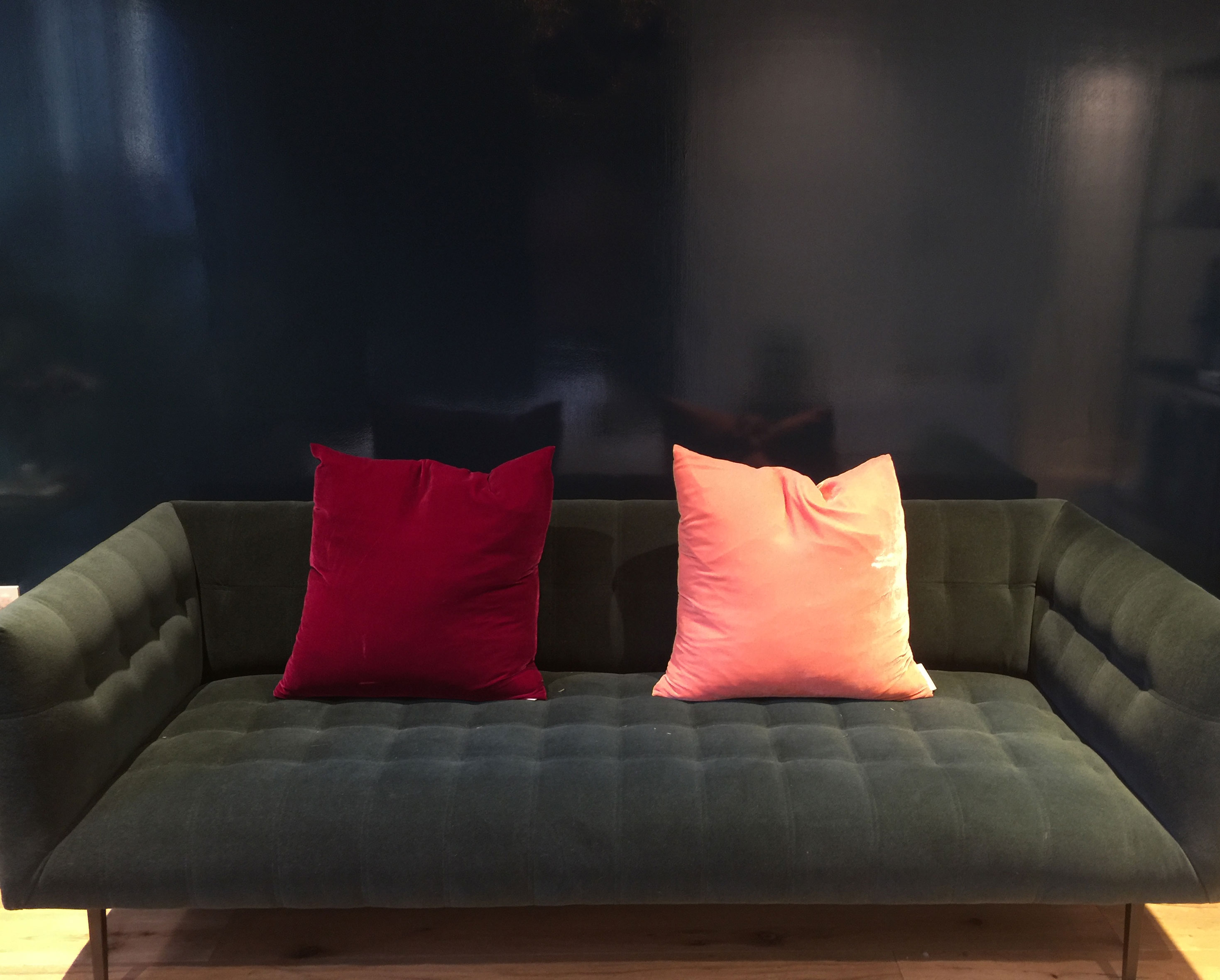 a red and peach pillow on a dark sofa in front of a dark blue wall