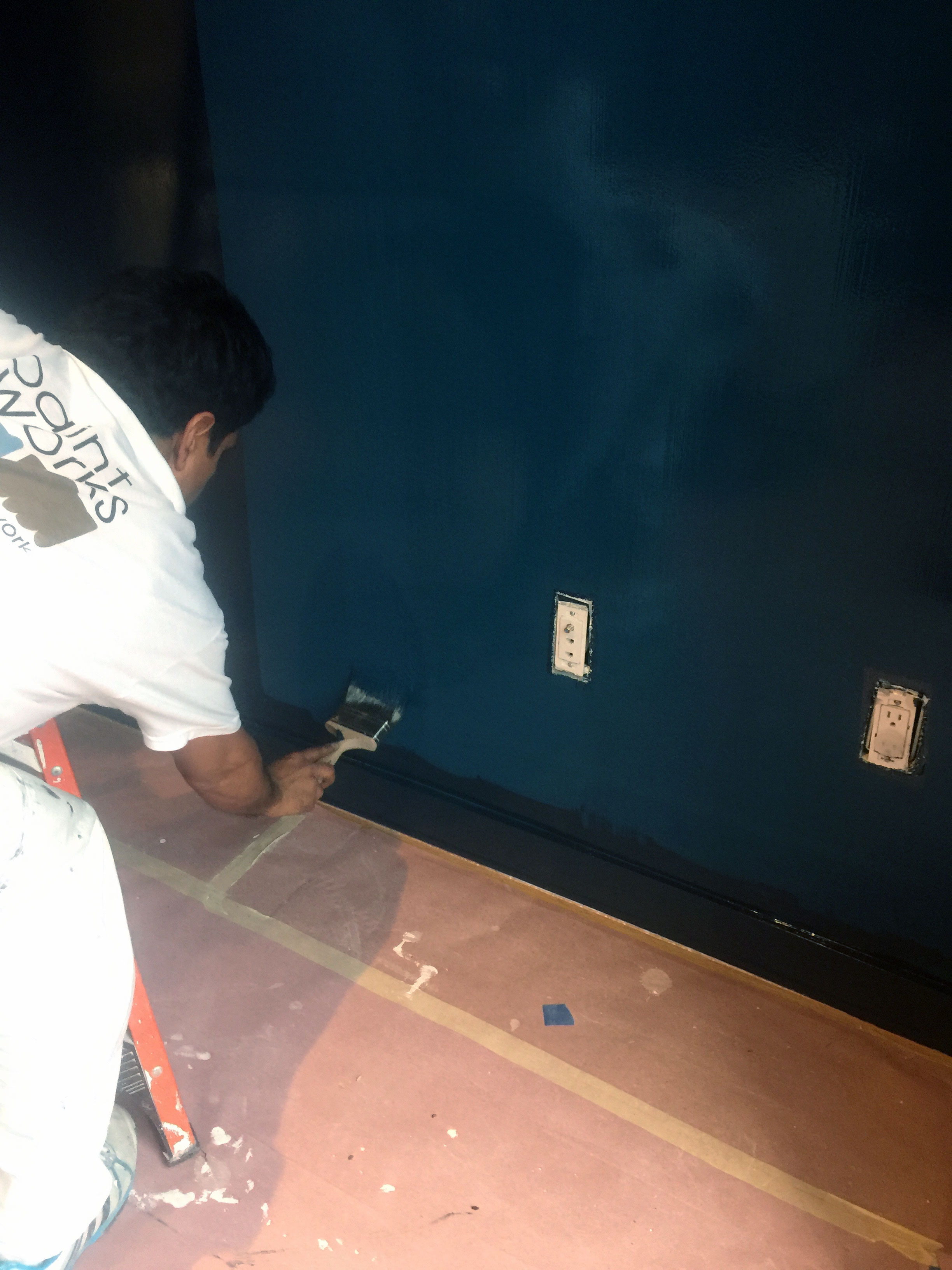 painter painting a wall dark blue with a brush
