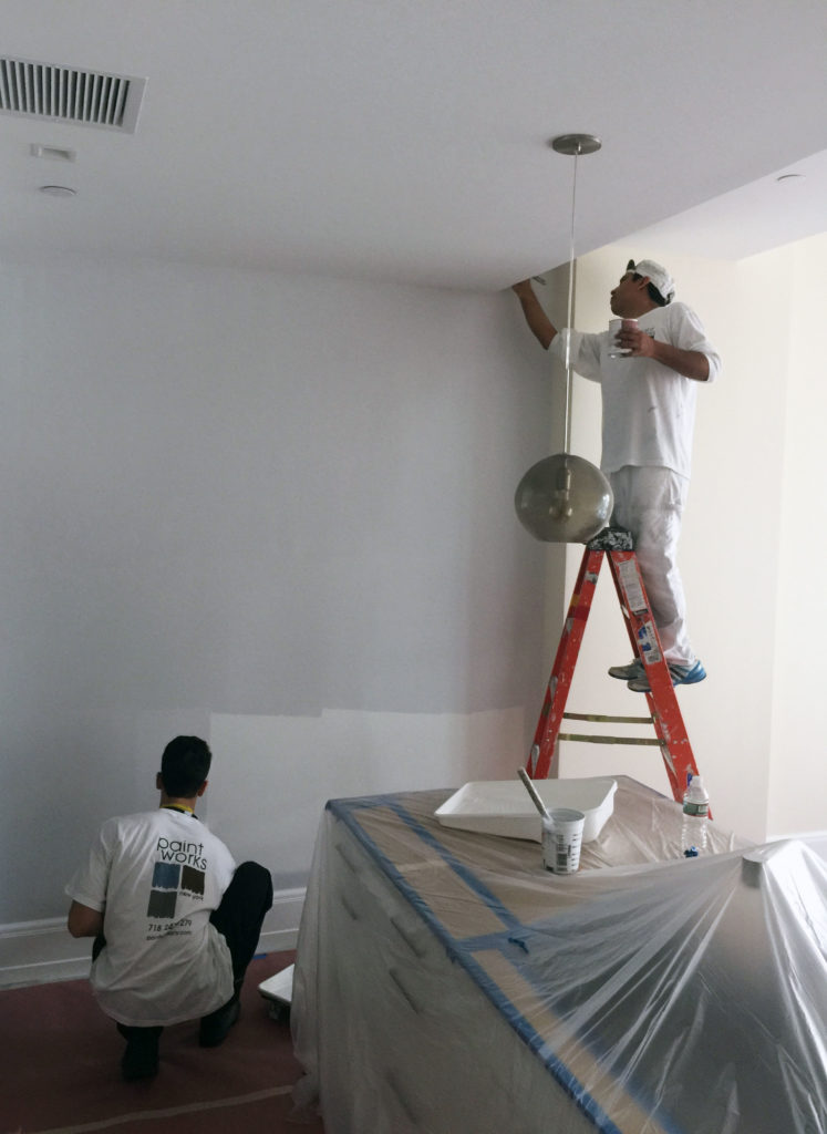 two painters painting a wall white one is on a ladder