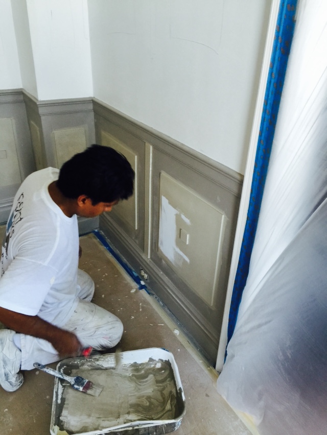 Worker painting an interior wall panel gray