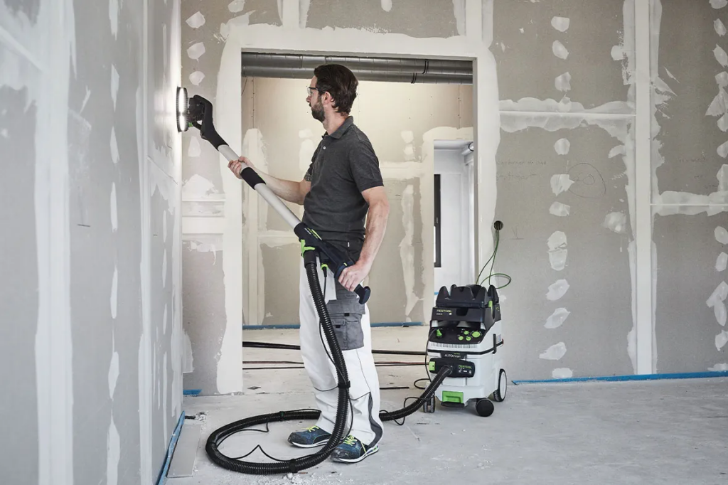 Photo of a drywalled using a Festool sanding and dust extraction system to finish a wall