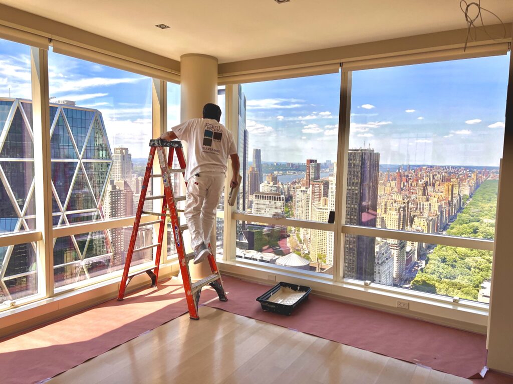 A interior painter working in front of windows overlooking New York City