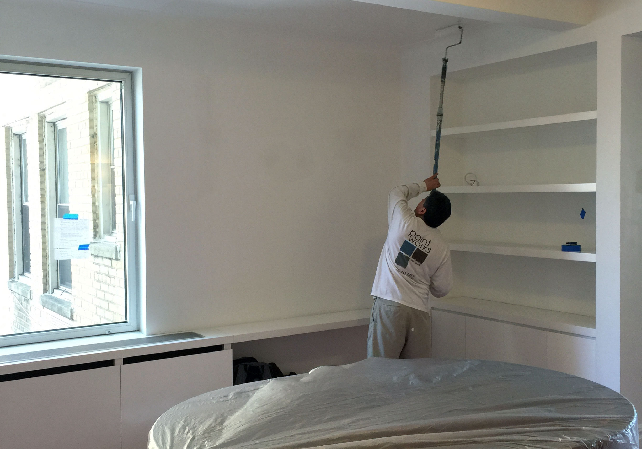 worker using an extension roller to paint a wall