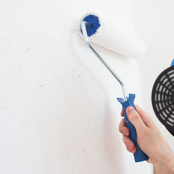 Man holding a small paint roller wearing a respirator for painting